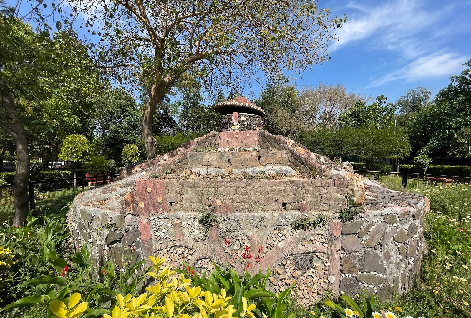 A Block Park in Ashok Vihar: ornate stone mosaic monument with a tiered roof, ringed by flower beds and trees
