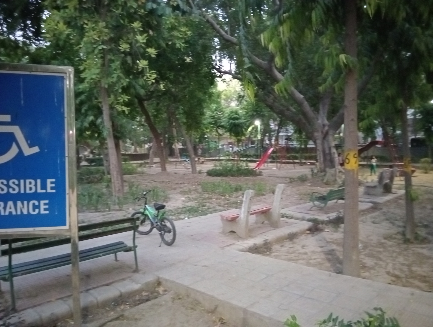 Hanuman Park at dusk: benches and a bicycle beneath leafy trees with a children's slide on the path