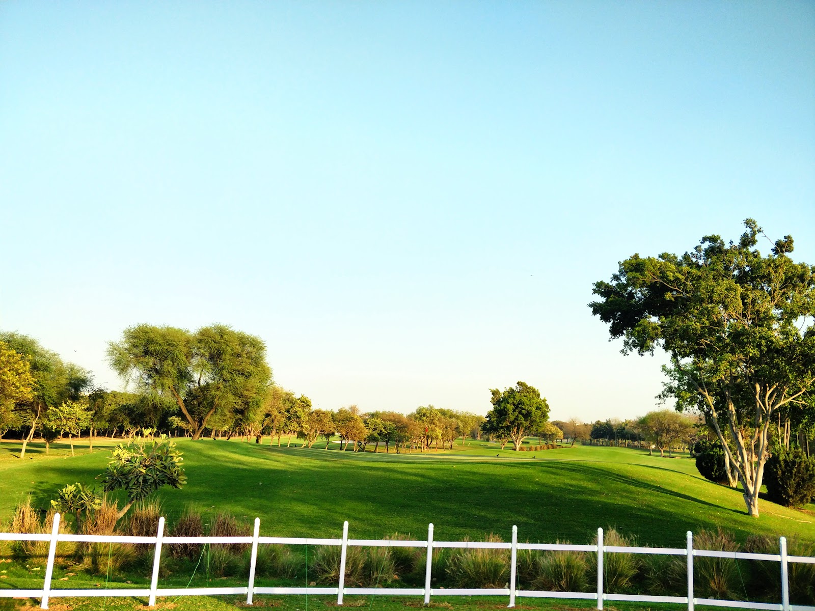 Manicured fairway and greens of Qutab Golf Course behind a white boundary fence