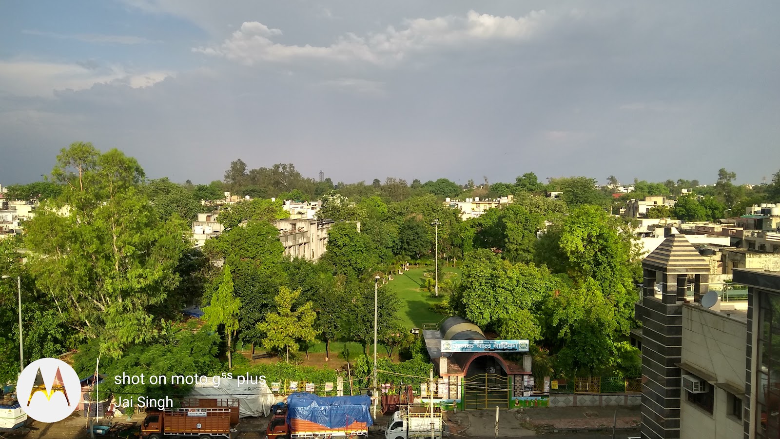 Radhe Park on a sunny morning: paved walking path bordered by trimmed hedges, lawns and palms