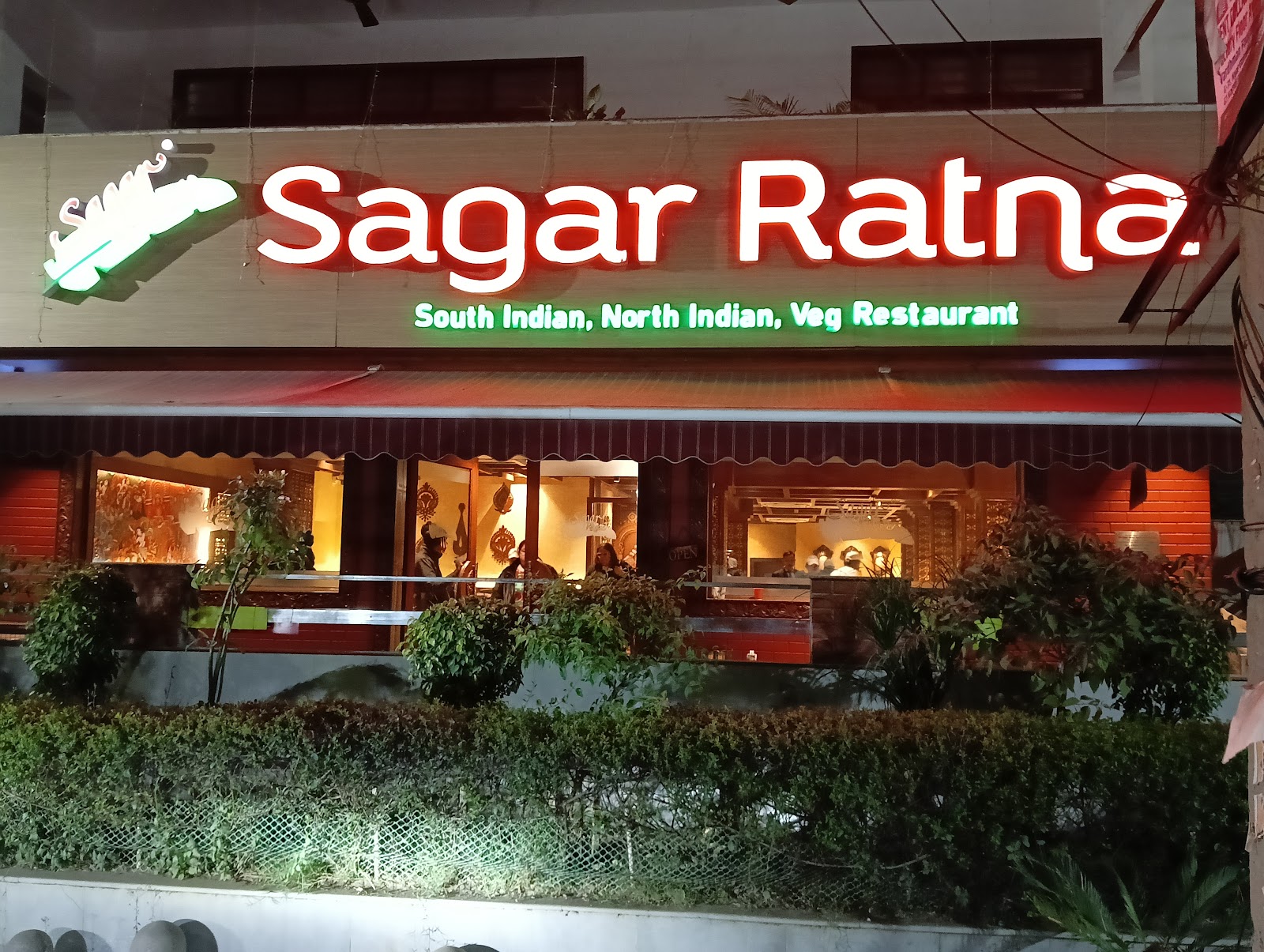 Illuminated Sagar Ratna storefront signage at night advertising South Indian, North Indian and vegetarian food