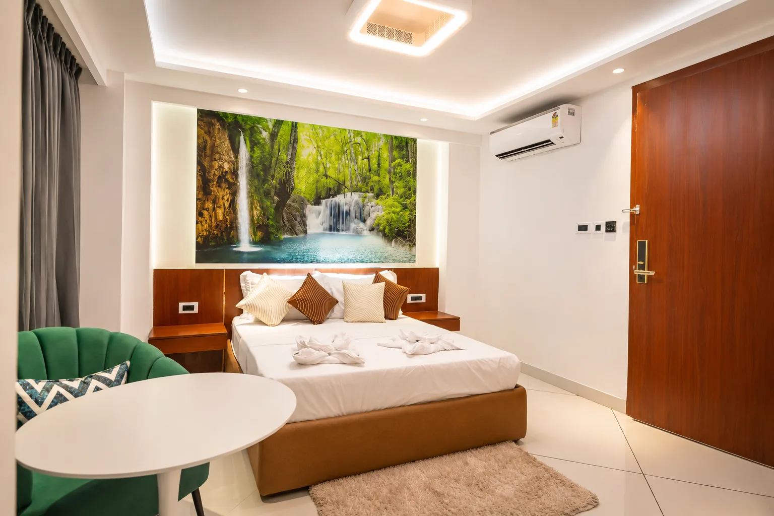 J60 Suites bedroom with a lush forest waterfall mural behind the bed and a green velvet armchair