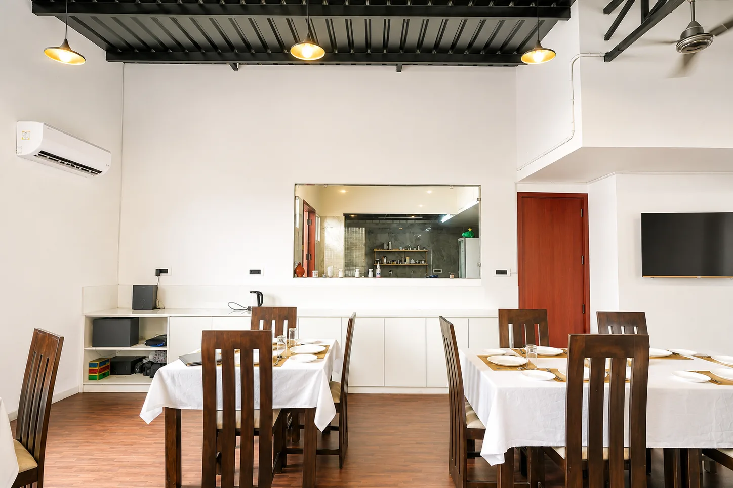 Homely dining area at J60 Suites Delhi — amber pendant lights over set tables beside the kitchen pass-through window.