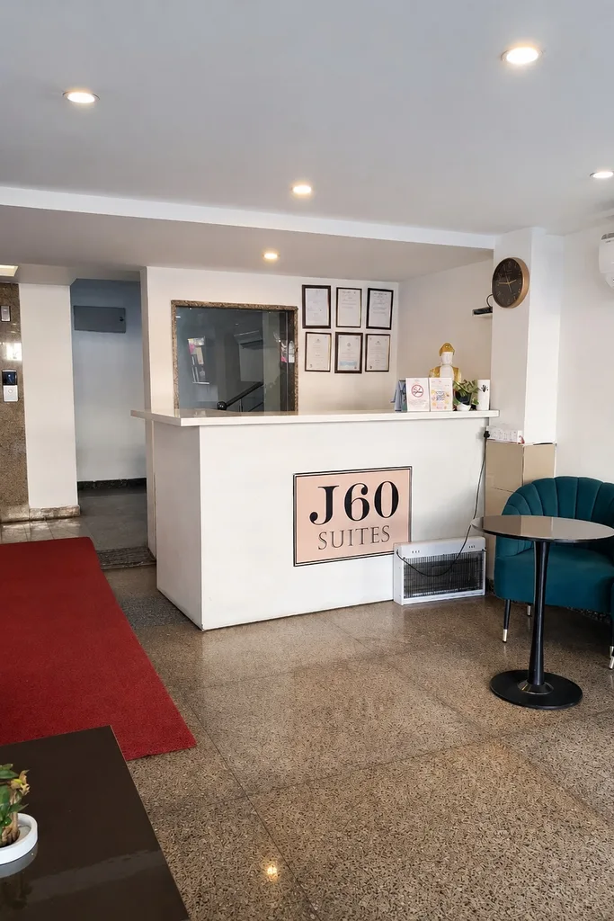 The reception desk at J60 Suites with the J60 Suites sign, teal armchairs beside it